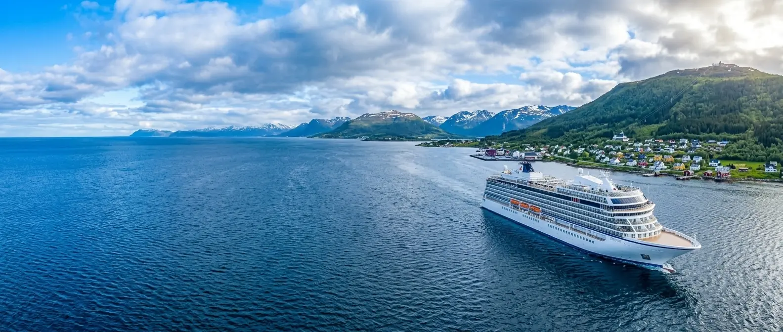 A cruise ship under way in a Norwegian fjord, passing a village below green mountains