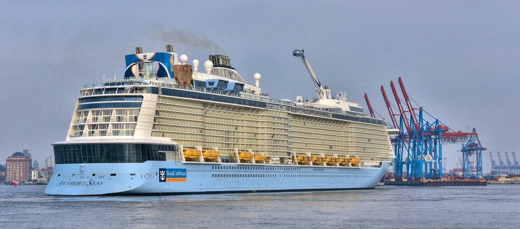 The Anthem of the Seas in front of a cityscape and shipping yard