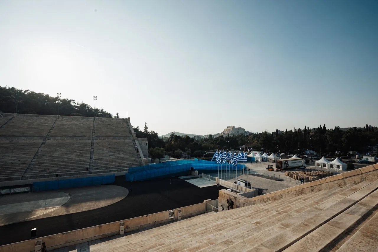 Panathenaic Stadium in Athens, Greece, with Acropolis and Greek flags visible.