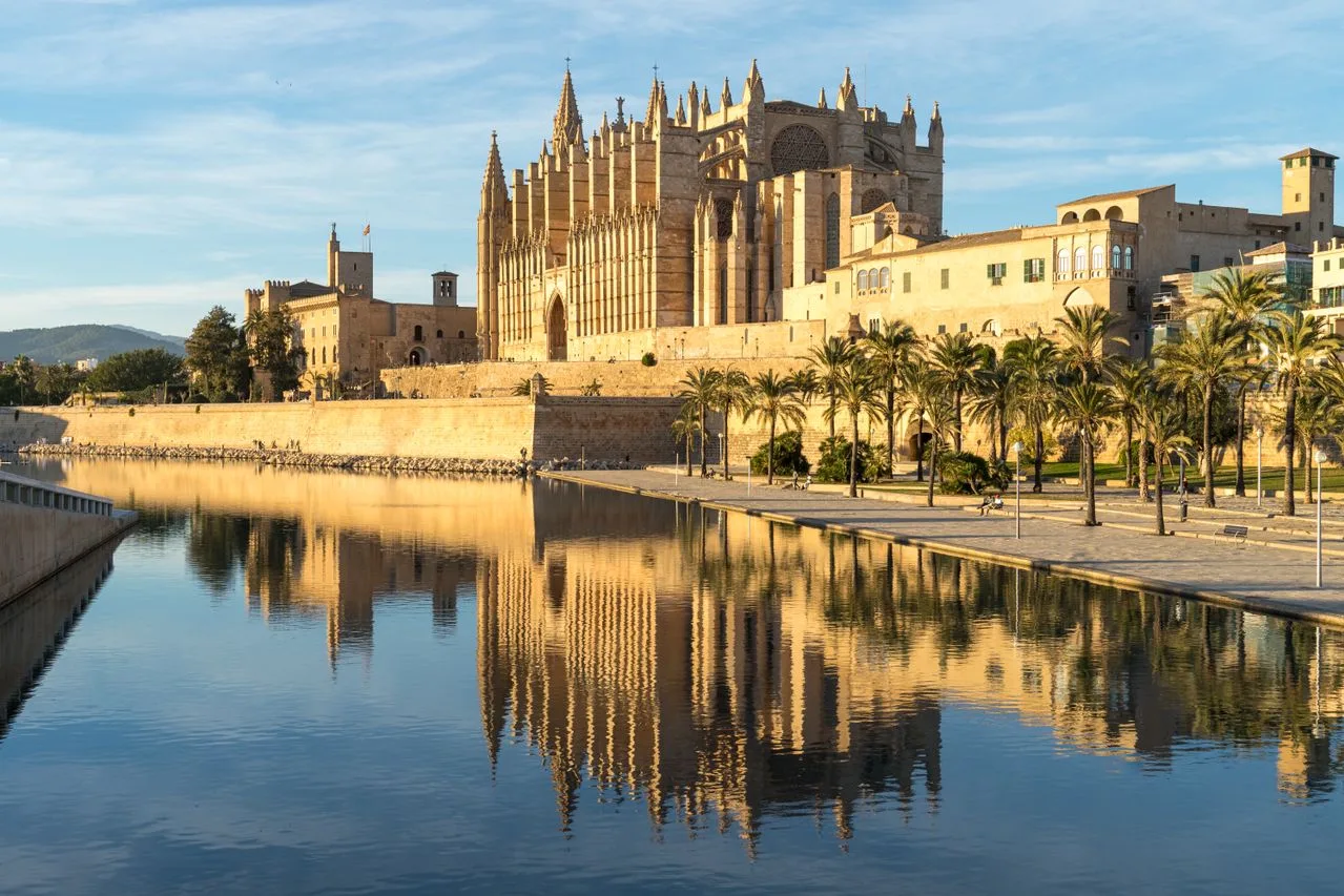 Gothic La Seu Cathedral in Palma de Mallorca reflects in a tranquil waterway.
