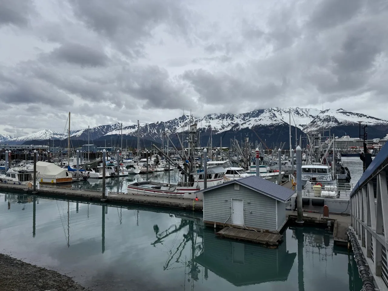 Scenic view of Seward Harbor with boats and snowcapped mountains under cloudy skies.