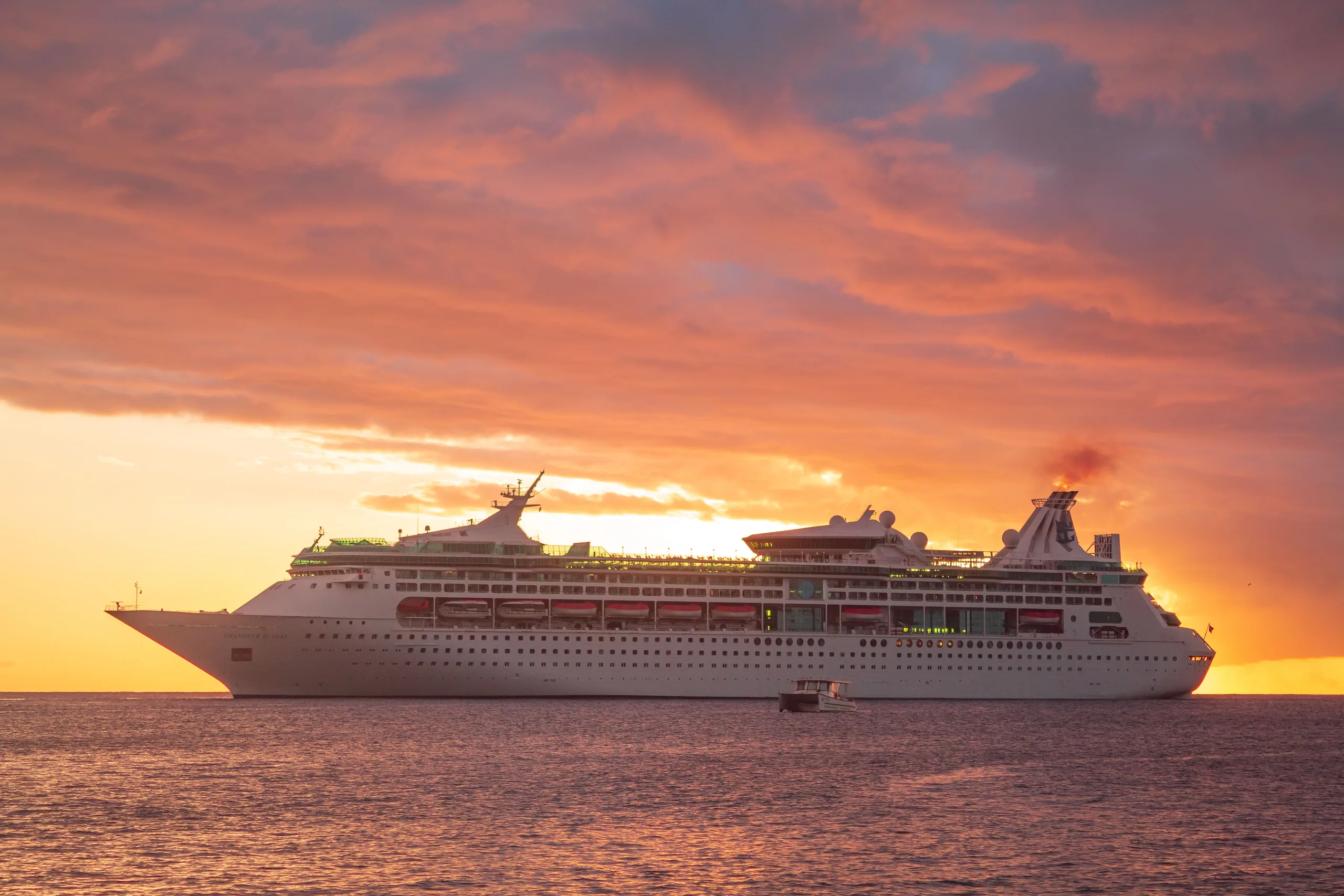 A majestic cruise ship sails across the Caribbean Sea at sunset in Grenada, showcasing a vibrant orange sky