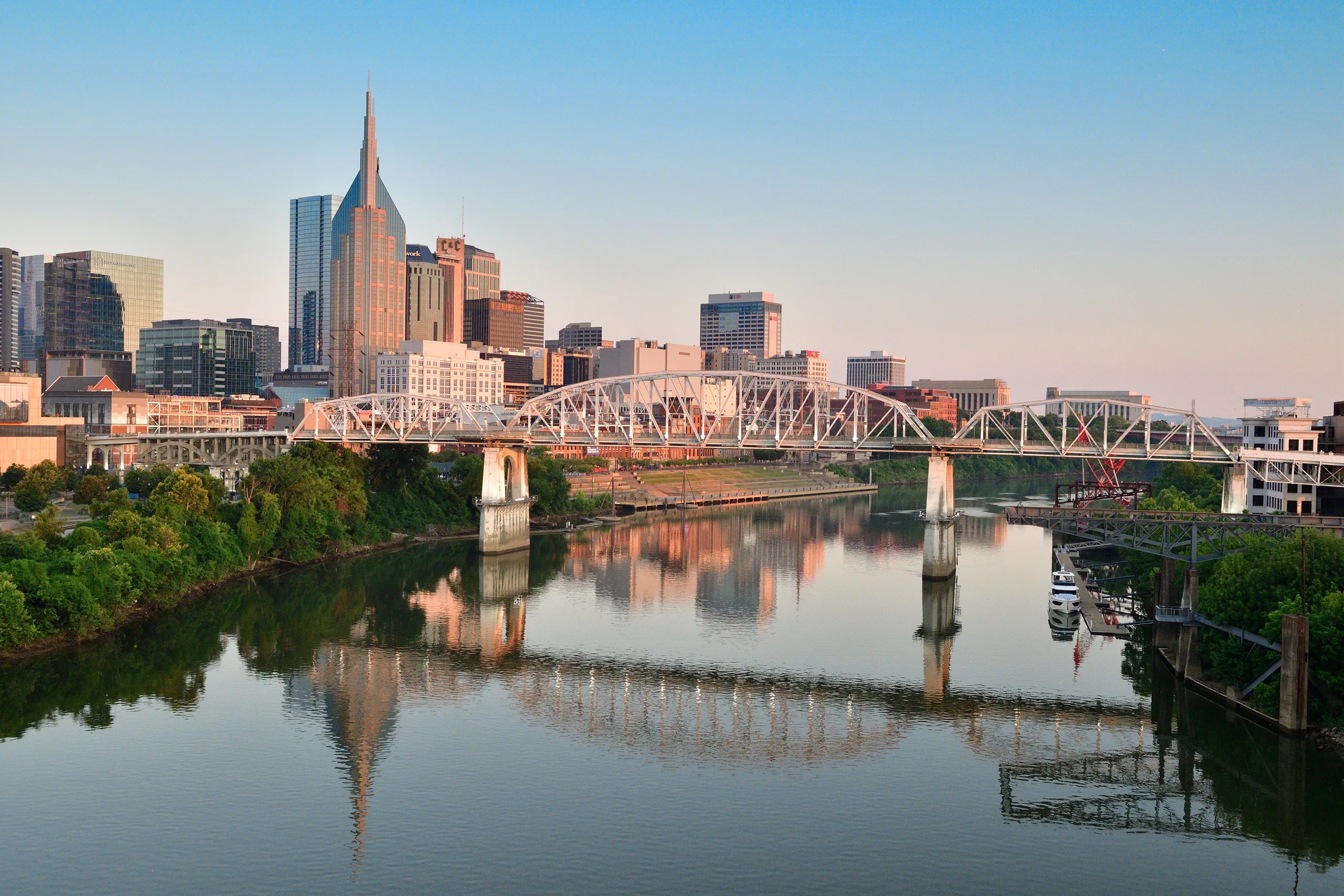 Scenic view of Nashville skyline and pedestrian bridge reflecting in the Cumberland River at sunrise.