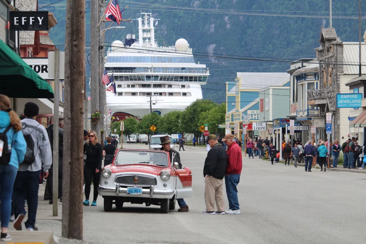 Vibrant street scene in Skagway, AK featuring a cruise ship and lively crowd.