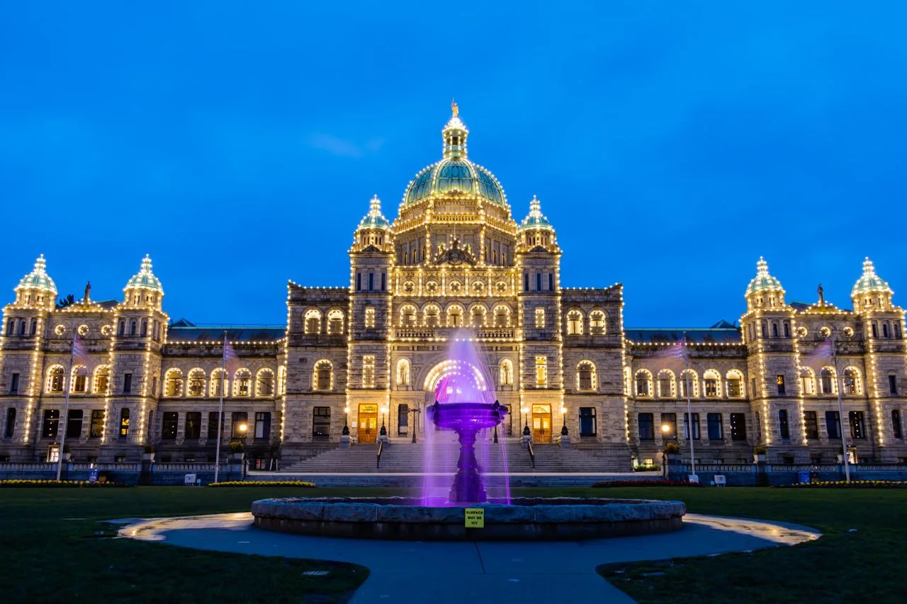 Stunning night view of the British Columbia Legislature Building in Victoria, Canada with glowing lights and a vibrant fountain.