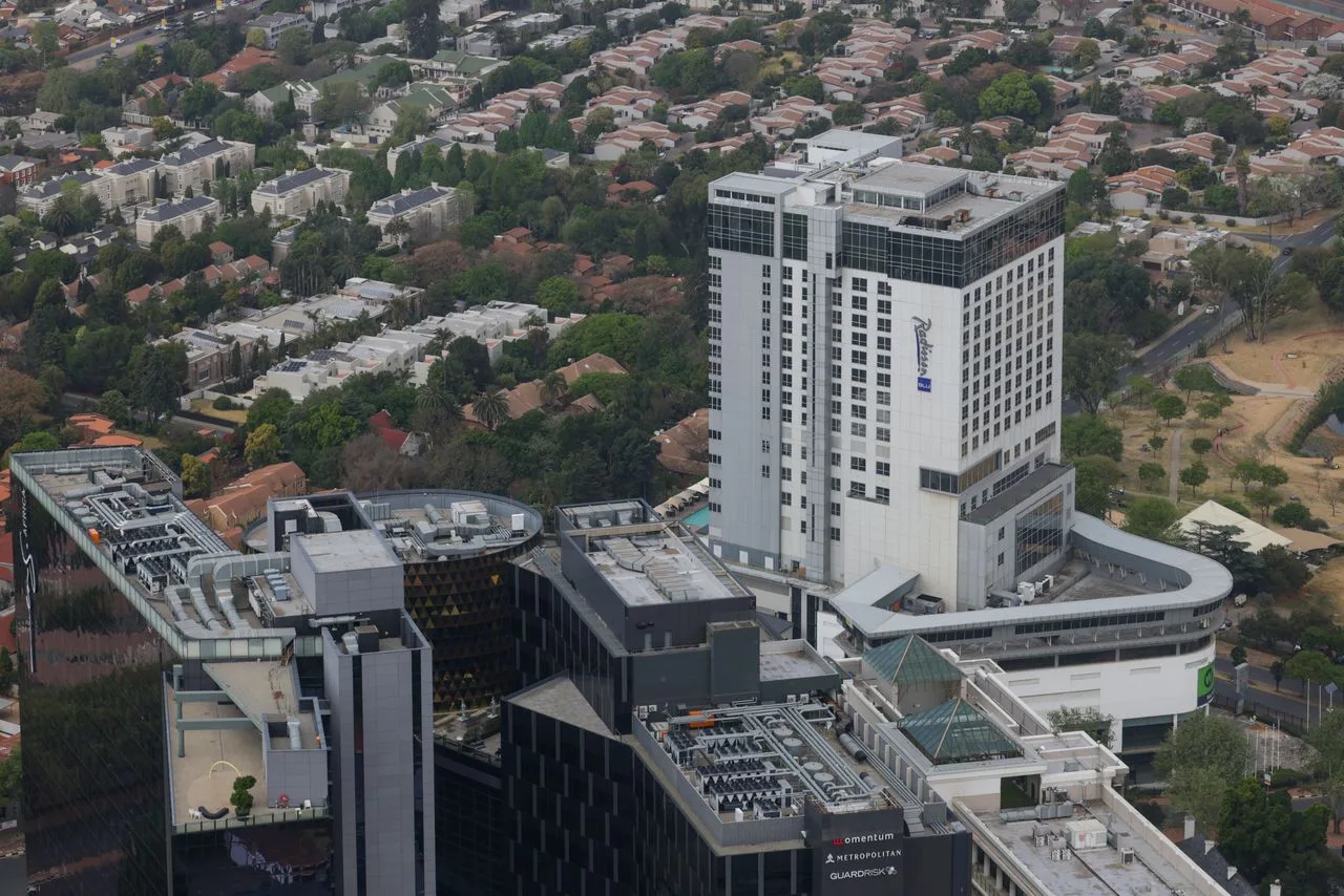 Aerial cityscape featuring modern buildings juxtaposed against suburban homes and greenery.