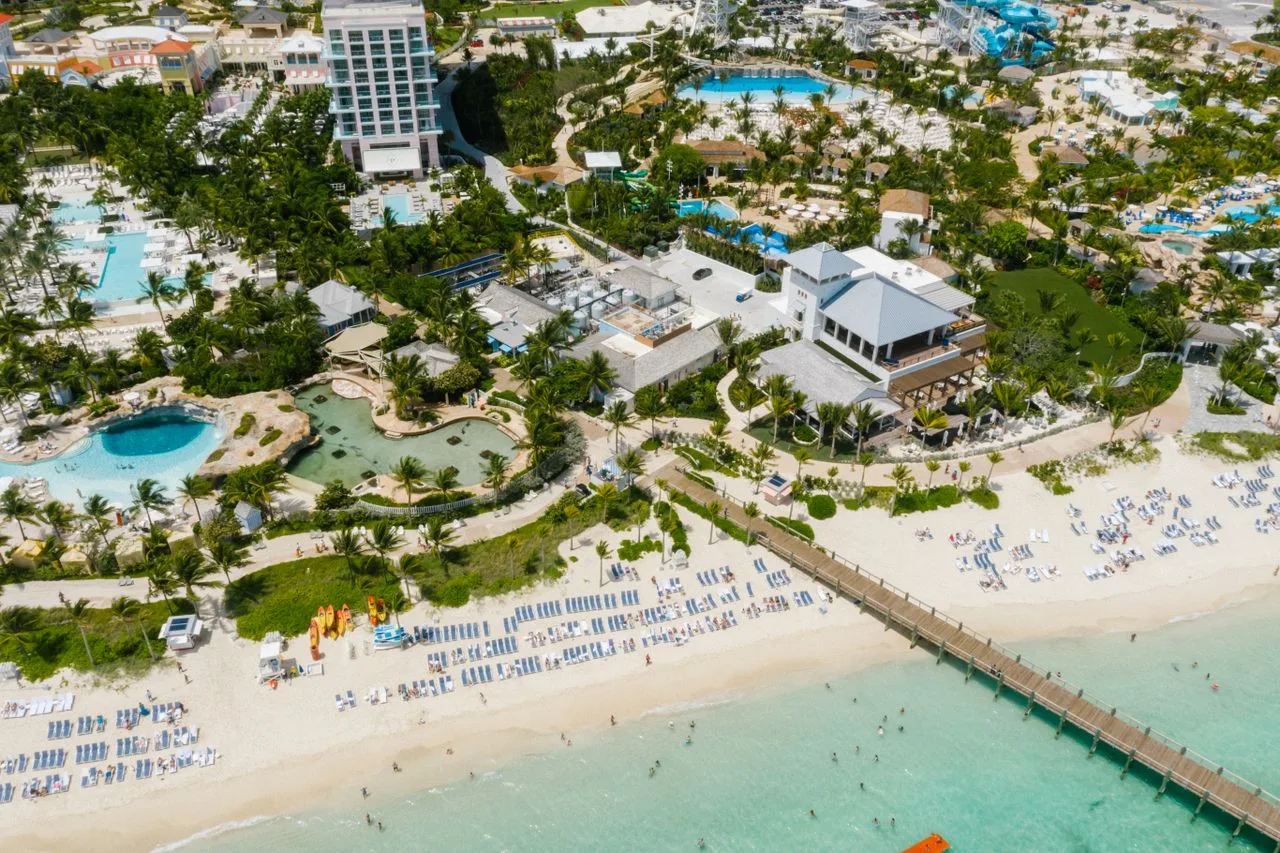 An aerial shot of a vibrant beach resort with clear waters, lush greenery, and modern architecture.