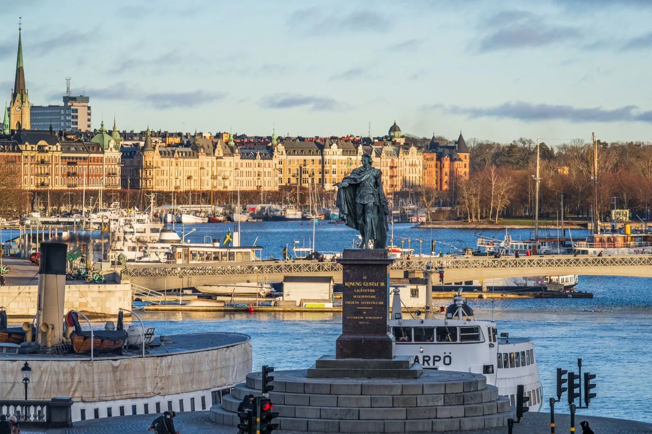 Gustav III statue with Stockholm's historic waterfront and skyline in winter sunlight.