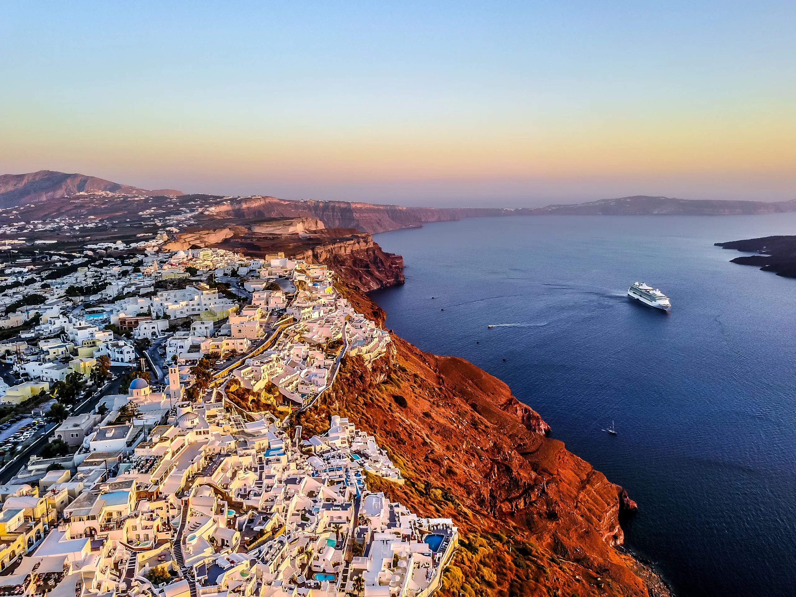 Stunning aerial shot of Santorini coast at sunset with a cruise ship in the Aegean Sea
