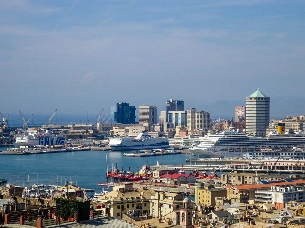 A stunning aerial view of Genoa's bustling harbor and modern skyline under a clear blue sky.
