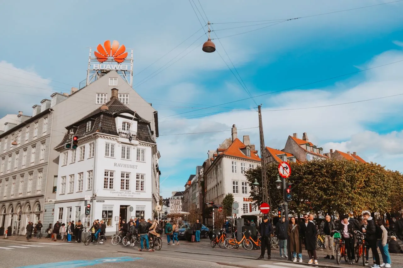 View of a busy street in Copenhagen, Denmark featuring pedestrians and historic buildings under a bright sky.