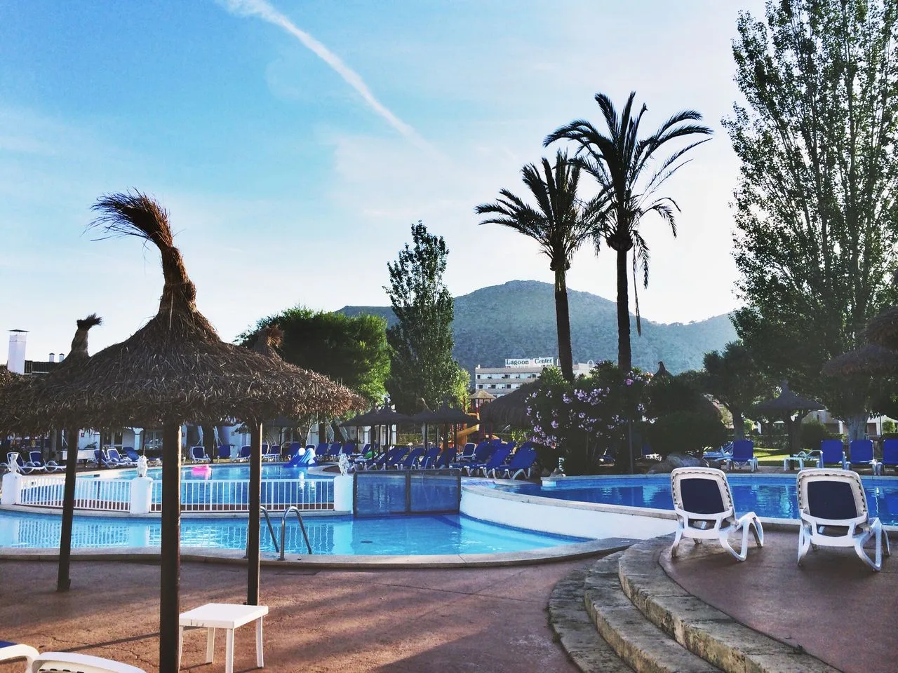 A serene tropical resort pool area with palm trees and sun loungers, ideal for relaxation and vacation vibes.