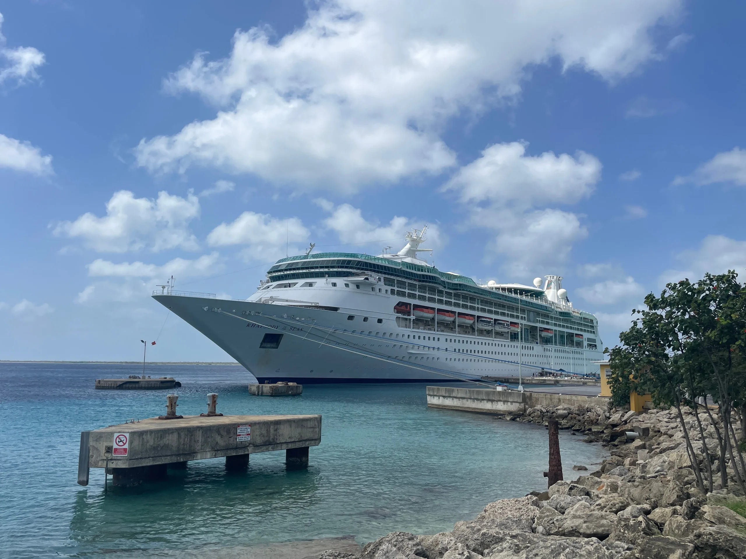 A luxurious cruise ship docked in a crystal clear tropical harbor, under a bright blue sky.