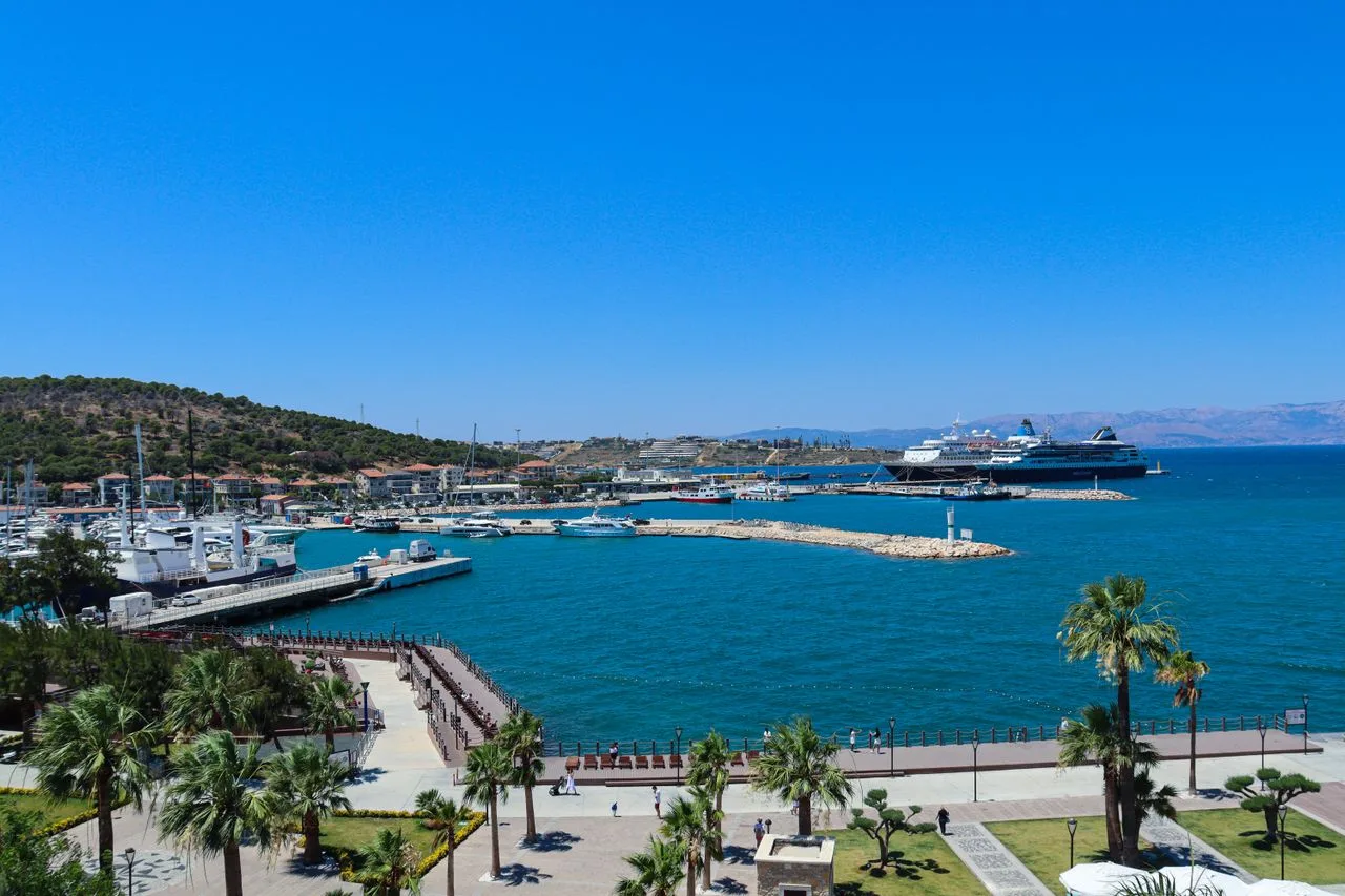 Stunning view of a Mediterranean harbor with yachts, cruise ships, and palm trees under a bright blue sky.