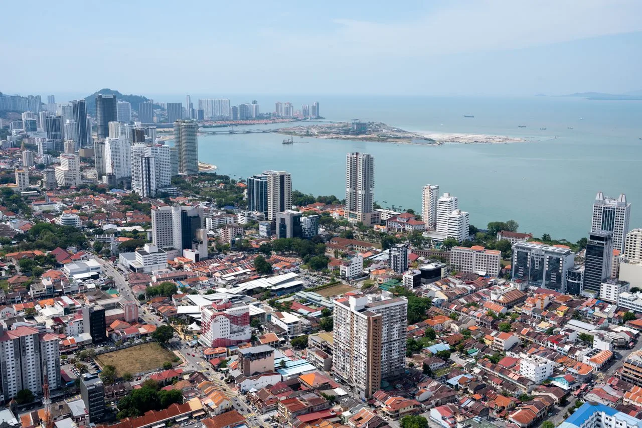 A vibrant aerial view of Penang's urban skyline with a coastal backdrop, showcasing modern architecture.