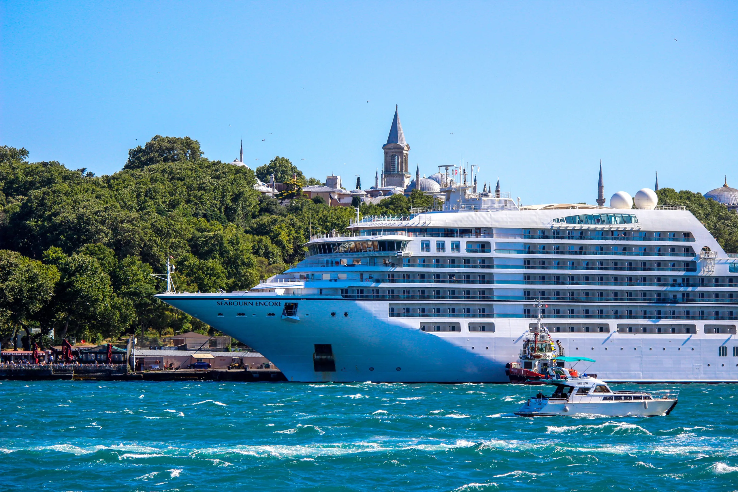 A majestic cruise ship sails through the Bosphorus Strait with a historic Istanbul skyline in the backdrop.