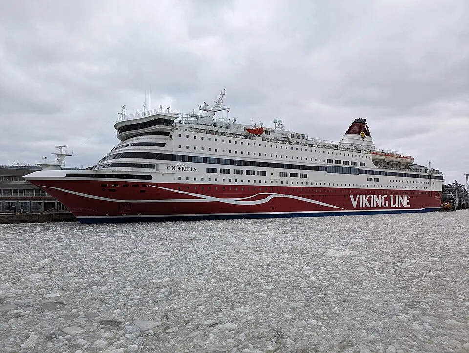 A large red and white ferry named "Viking Cinderella" docked in water filled with broken chunks of ice. The Viking Line vessel features multiple windowed decks and a red smokestack, set against a grey, overcast sky.